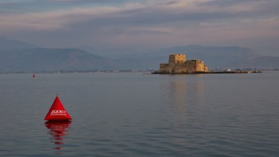 Bourtzi island fortress, historic castle in the evening light on the water with a red buoy,