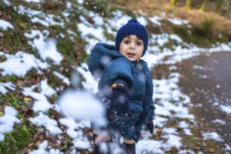 Young boy wearing a blue knitted hat and warm winter jacket, actively playing and throwing a
