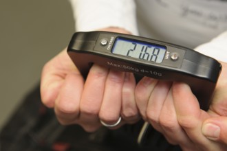 Woman holding hand scale for weight of suitcase travel bag flight luggage checks luggage weight for