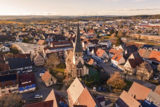 Bird's eye view of a village with a distinctive church tower and surrounding settlement in autumn,