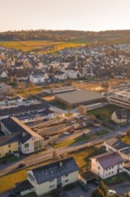 Aerial view of a suburb with buildings and roads in warm sunset light and surrounding hills,