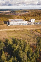Factory building next to forest and clearing, behind a village on a hill in autumn tones, new