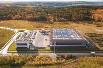 Large factory with parking lot, surrounded by forest and open spaces in an autumnal setting, new
