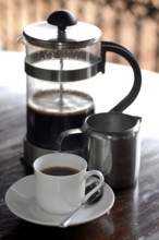 French coffee press next to a cup of coffee and a milk jug on a table, Serenity boutique hotel,