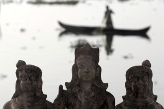 Three Hindu god statues made of clay, fishermen in a boat in the background, Vembanad Lake, Kerala,