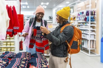 Happy young multiracial couple smiling as they browse and select red holiday sweaters in a busy