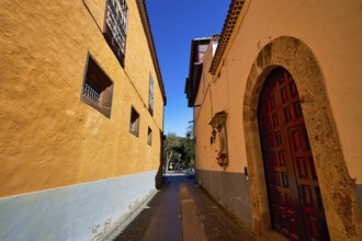 Narrow historic alley with yellow facades and wooden doors in the shade of a wall, UNESCO World