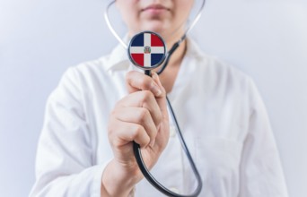 Female doctor holding stethoscope with Dominican Republic flag. National health system of Dominican