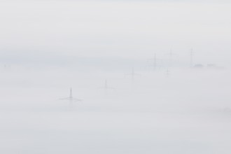 High-voltage pylons rise up from the thick sea of fog, silence and technology the silhouette of