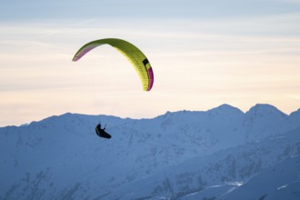 Paragliders flying over snowy mountain peaks in winter in evening light, KitzbÃ¼hel Alps, Tyrol,