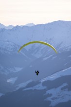 Paragliders flying over snowy mountain peaks in winter in evening light, KitzbÃ¼hel Alps, Tyrol,