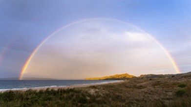 Landscape with sea and sandy beach in New Zealand with rainbow, in the evening at golden hour.