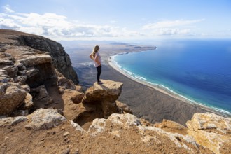 Young woman enjoying the view from the Risco de Famara cliffs to Famara beach, Playa de Famara with