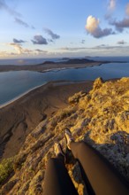 First person view, legs of a woman sitting on a steep cliff, view of the sea and the island of La