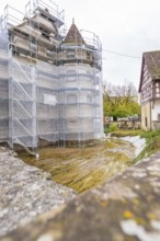 A medieval tower with scaffolding near a half-timbered house, both under renovation, Wasserschloss