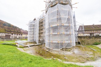 A rural-style renovated building with scaffolding and tarpaulins, surrounded by green spaces,