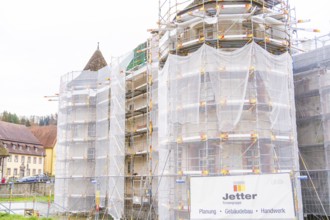 Side of a building with several towers surrounded by large scaffolding for restoration,