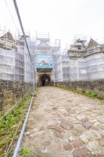 Paved path leads to a scaffolded entrance gate of a converted medieval building, Wasserschloss