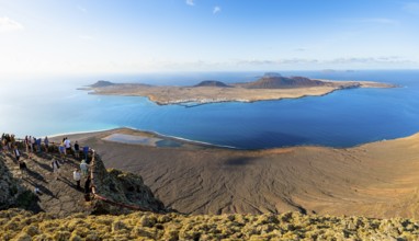 View of La Graciosa island with volcanic craters in the evening light, tourists on an observation