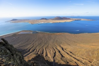 View of steep cliffs by the sea and island of La Graciosa with volcanic craters in the evening