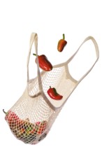 Colourful sweet bell peppers fall into an eco-friendly string bag isolated on white background