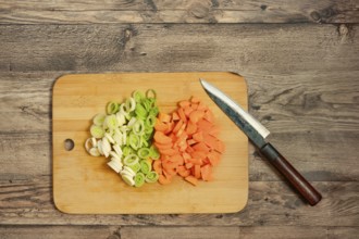 Fresh leek onion and carrots are chopped and neatly arranged on a wooden cutting board. A sharp