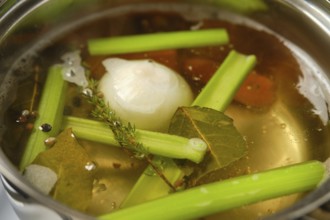 A pot simmers on the stove filled with water, celery stalks, onions, and spices. Fresh herbs like