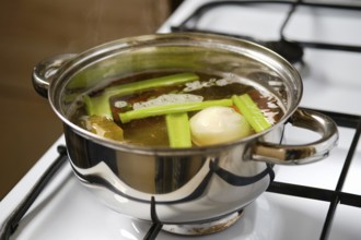 Fresh celery, carrot and an onion simmer in a pot of broth on the stovetop. The pot shows steam