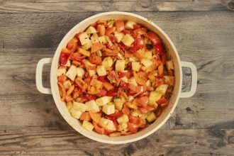 Chopped bell peppers, tomatoes, and onions are mixed together in a large pot, showcasing fresh