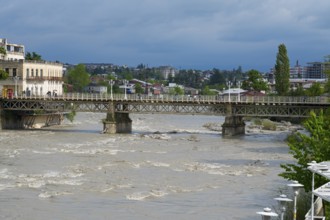 A rustic bridge across a river with an urban backdrop under cloudy sky, White Bridge over the Rioni