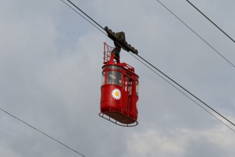 A red cable car cabin hangs against a cloudy sky, a dynamic mode of transport, Kutaisi, Imereti