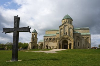 Historic church with cross in the foreground, cloudy sky surrounded by green landscape, Bagrati