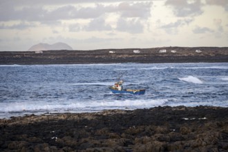 Fishing boat out to sea in the evening, seaside coast with volcanic rocks at sunset, La Santa,