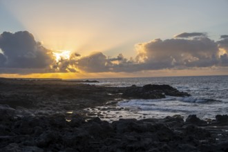 Dramatic cloudy sky with sunbeams at sunset, seaside coast with volcanic rocks, La Santa,