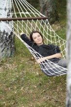 A young woman reclines comfortably in a hammock suspended between two trees