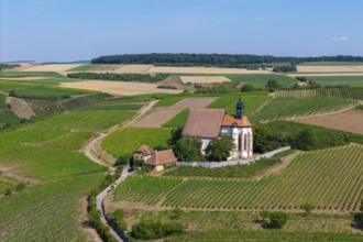 Pilgrimage church Maria im Weingarten, surrounded by green hills and fields under a sunny sky,