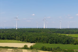 Several wind turbines on the horizon above a forest and fields, under a blue sky, near Volkach,