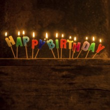 Brightly lit birthday candle arrangement spelling out Happy Birthday on a rustic wooden surface for