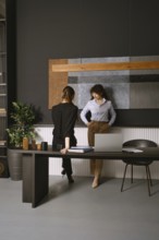 Two women discussing work in a modern office space with elegant decor and stylish furnishings