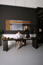 Two women engage in a productive meeting in a sleek office environment. One is seated at a desk,