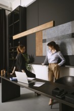 Two women engage in a productive discussion in a sleek office with dark walls and contemporary