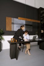 Two women are engaged in a collaborative work session in a stylish office environment. One woman