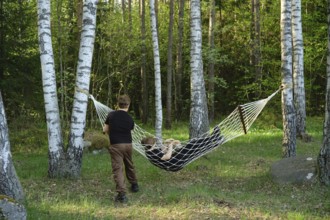 Two children enjoy their time outdoors, one relaxing in a hammock suspended between two trees while
