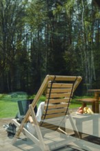 A person enjoys leisure time on a wooden lounge chair, surrounded by picturesque trees and a calm