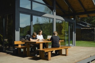 A family sits together at a wooden table on a sunny afternoon, engaged in various activities. One