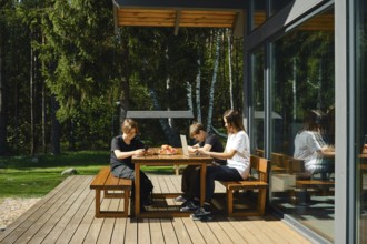 A single mother works remotely at a laptop sitting at a table on the terrace of a country house,