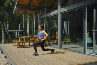 A woman in athletic wear practices lunges on a spacious wooden deck of a modern cabin. Surrounded