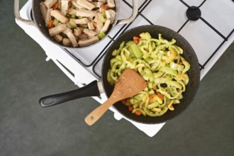 Fresh vegetables in a skillet on a stove and cooked meat chunks in another pan