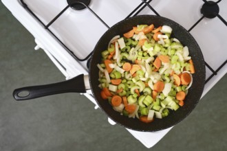 A skillet filled with freshly chopped onions, carrots, and celery sits on a gas stove. The vibrant