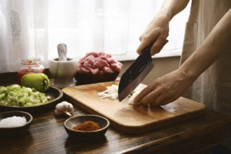 A chef finely chops onion on a wooden cutting board in a warm kitchen. Fresh ingredients like